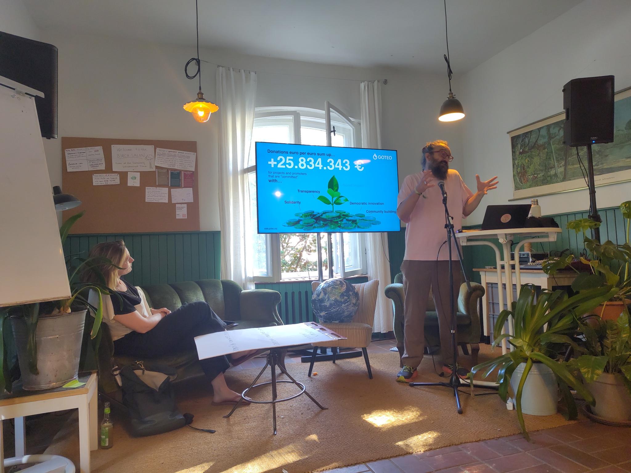 Olivier Schulbaum presenting the cadse of Goteo in front of a presentation slide showing the >25M€ mobilised from small donations to thousands of commons and civic projects